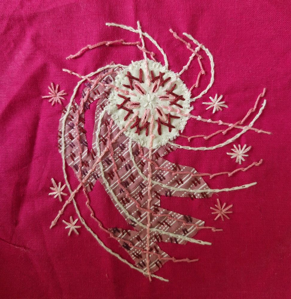 Spirals of cream and pink tendrils plus straight lines of coral stitch, all emanating from a cream circle. Behind the tendrils is a ragged scrap of fabric, stitched over haphazardly in dark red. The whole piece is on a hot pink background.
