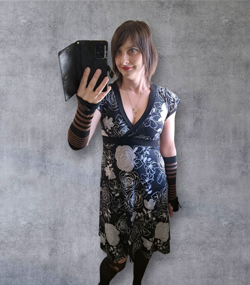 Mirror selfie from 🇨🇦 Thanksgiving. Wearing a black and white flower dress, black and brown striped arm warmers, and cat themed stockings. Background was replaced with a generic image.