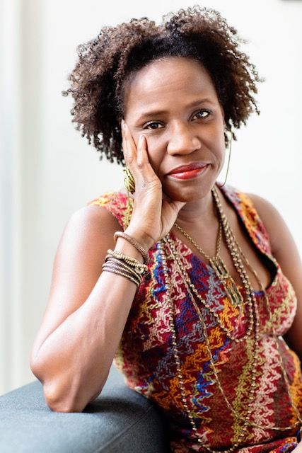 A photograph of Tina M. Campt, a black woman with short, dark hair dressed in a colourful dress with patterns in blue, pink and orange.  