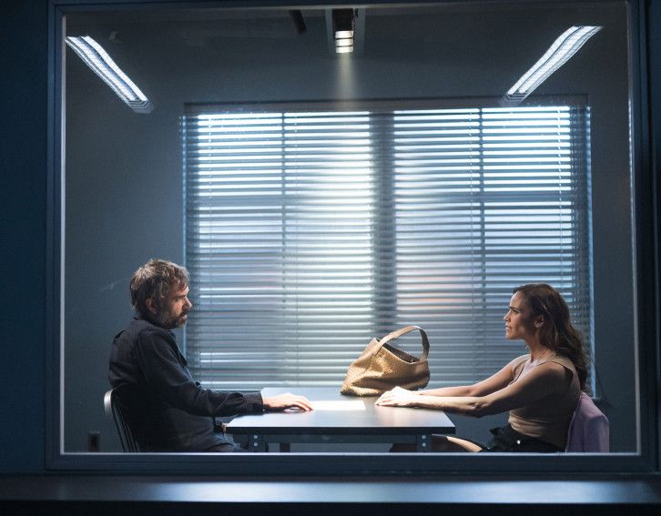 Rossif Sutherland sits at a table facing Paula Patton, who is seated opposite him with a purse on the table beside her outstretched arms.