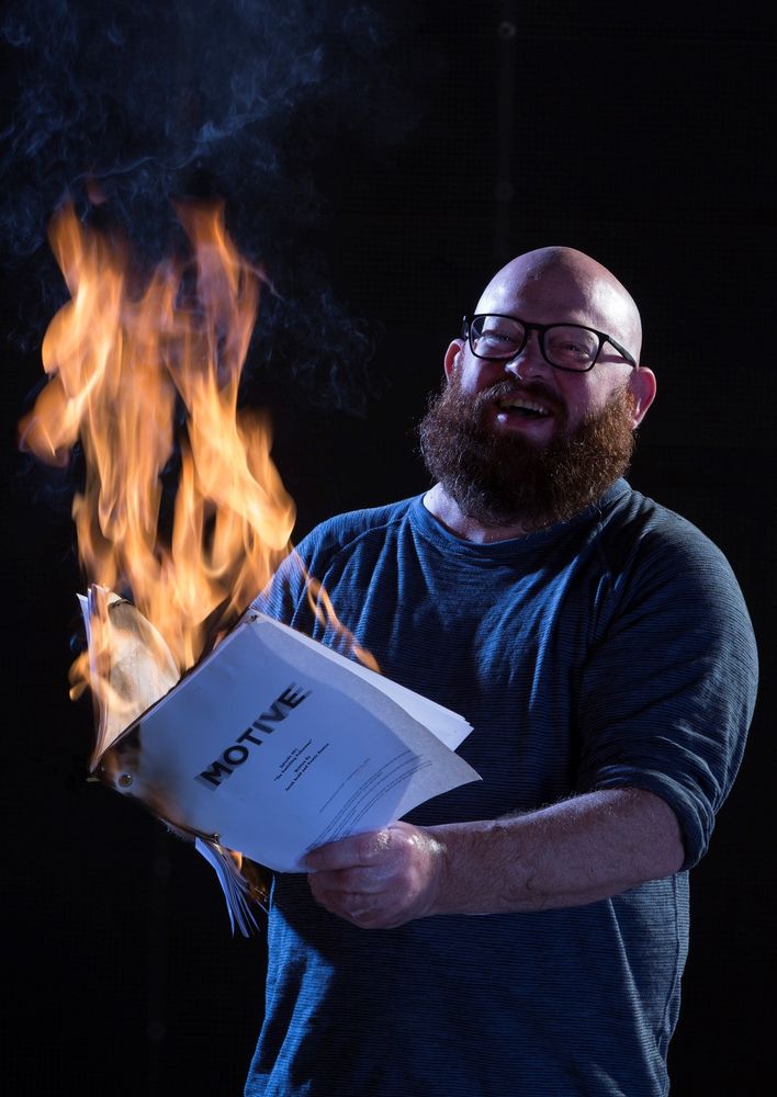Dennis Heaton laughs while holding a burning script for the TV series Motive. 