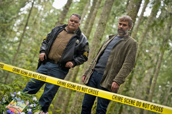 Aaron Douglas and Rossif Sutherland stand in the woods behind crime scene tape and look toward the ground.