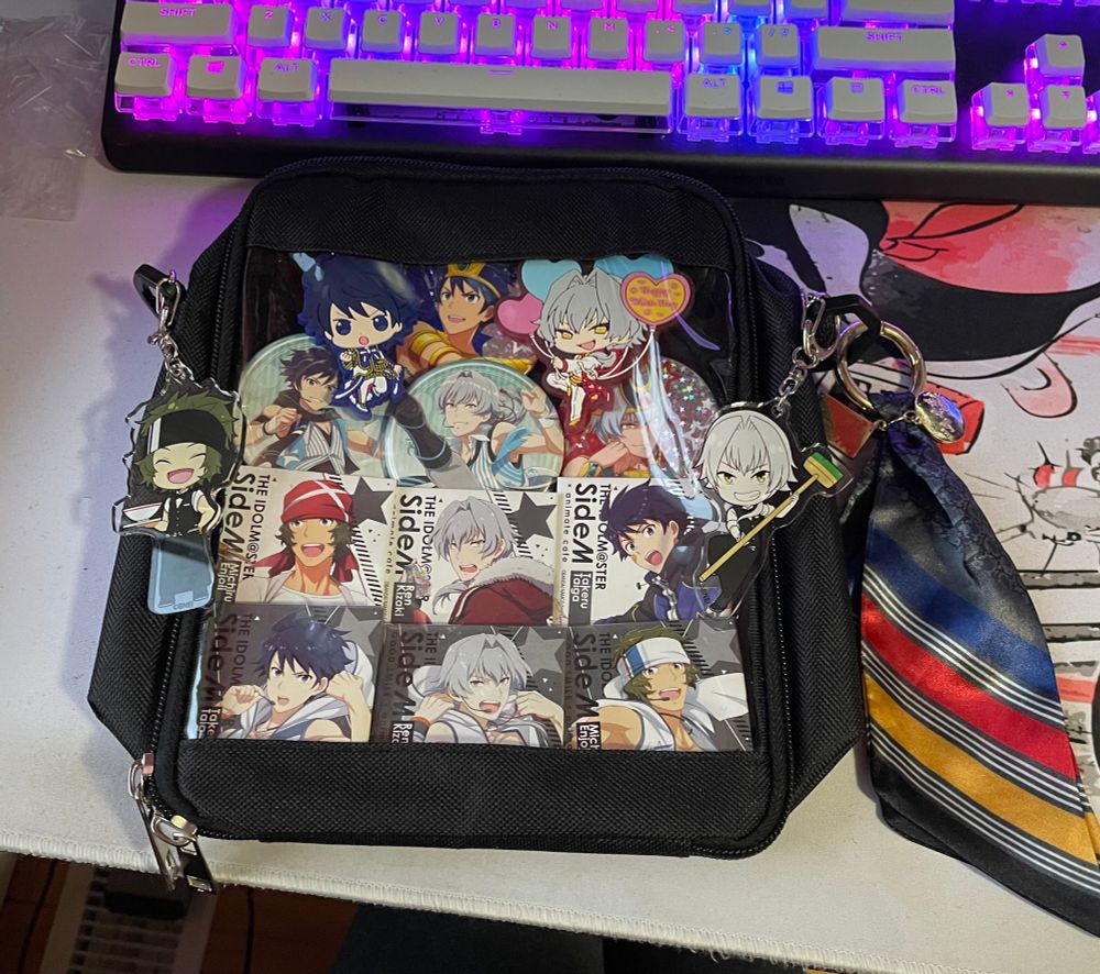 A small black shoulder bag showcasing can badges and keychains of characters from Idolm@ster Sidem music group The Kogadou