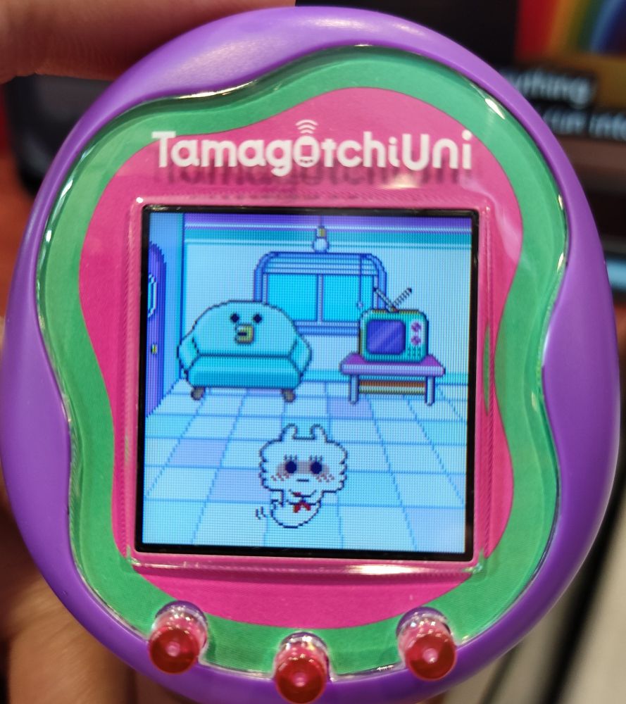 close up photo of a purple tamagotchi uni with a shy personality lionetchi on the screen