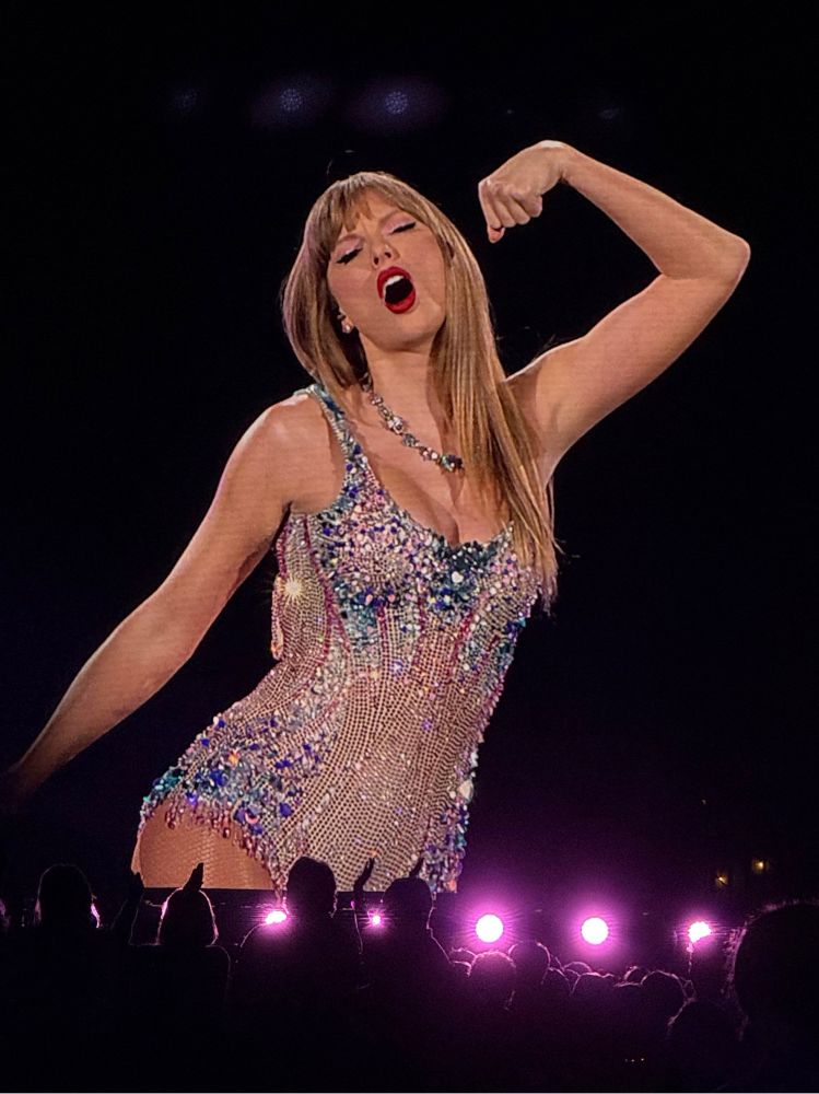 My photo of Taylor Swift at the Eras tour, wearing the pink and blue “Lover” bodysuit, posing with one bicep flexed and her mouth open