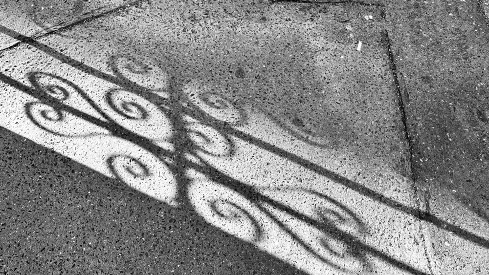 Stín mříže dopadá na chodník na pražských Vinohradech