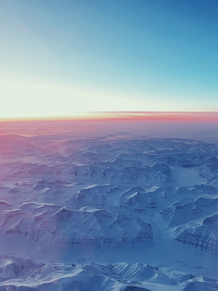 Low sunset from airplane over Greenlands icy mountains 