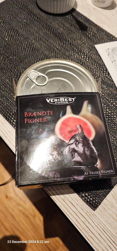 A tin with a ring pull, in a box labelled "burnt figs" in Norwegian. Box is sat on a faux wooden table.