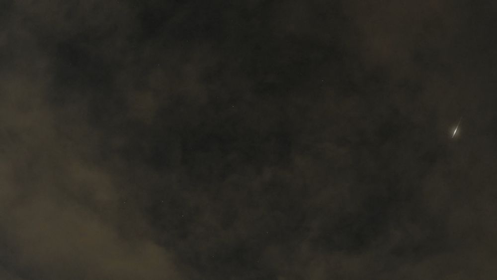 Cloudy night sky with a meteor flash near the right hand edge. Stars faintly visible behind yellow clouds.