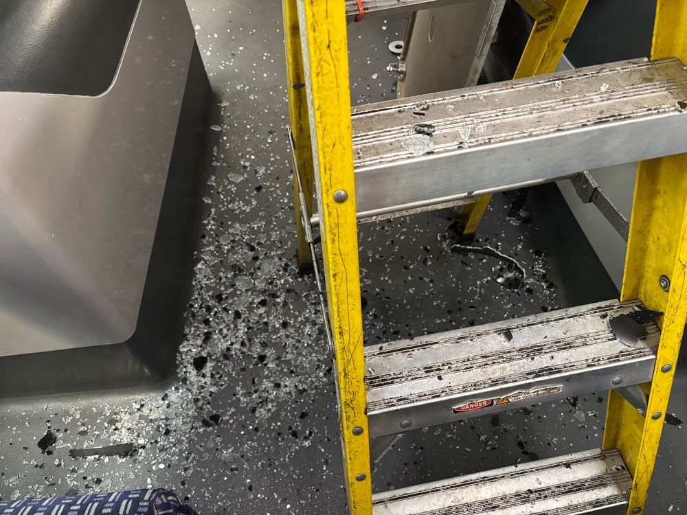 Broken glass on the floor with a set of yellow metal stepladders. 