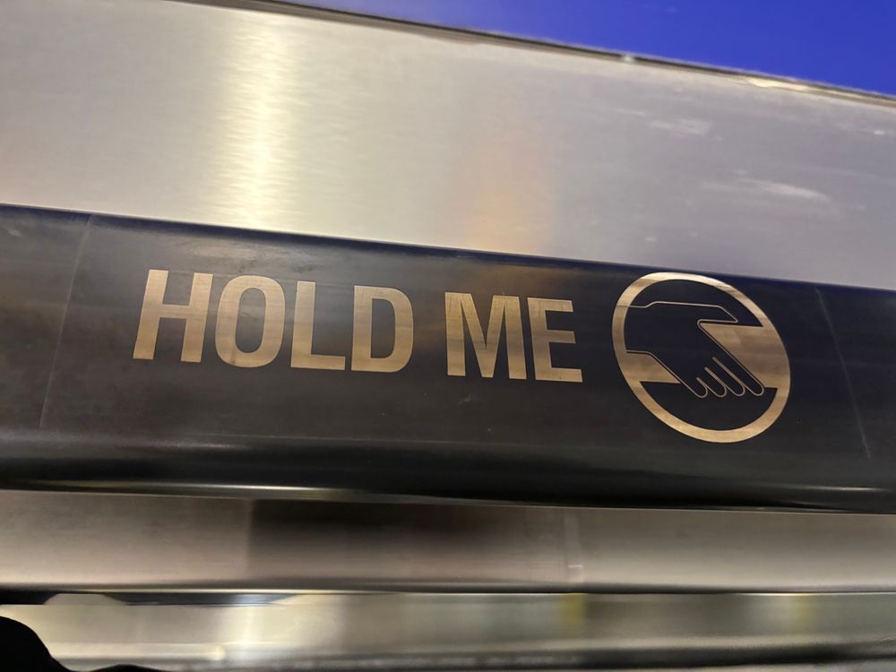 Escalator handrail with ‘hold me’ in gold text.