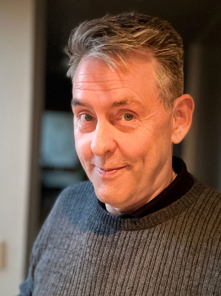 Smooth-faced man with deep dimples is smiling sardonically. 