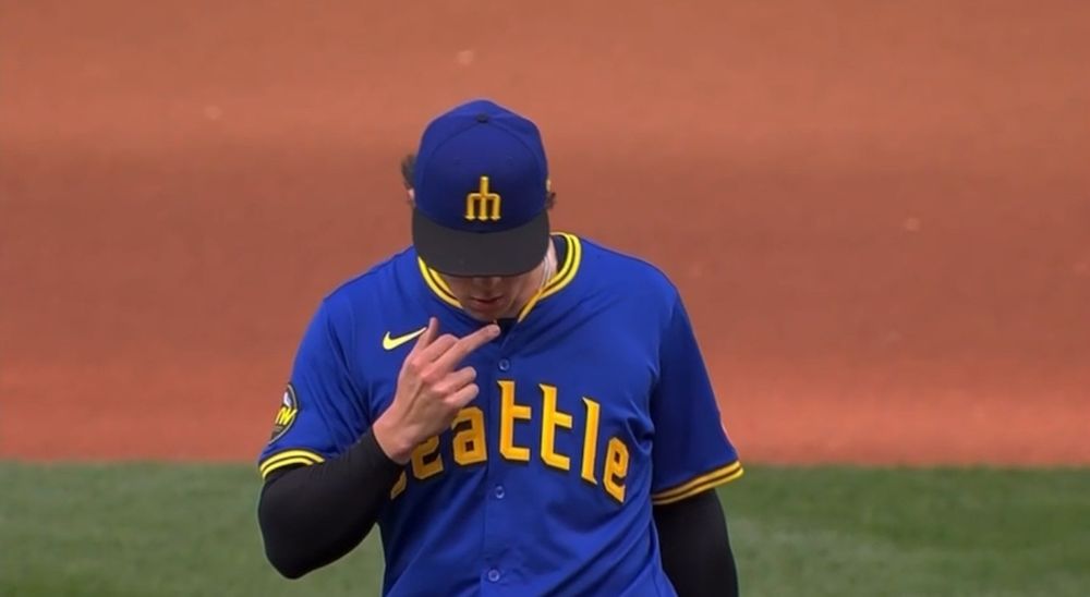 Bryan Woo walking off the mound, head down, giving a not-so-furtive middle finger with his right hand
