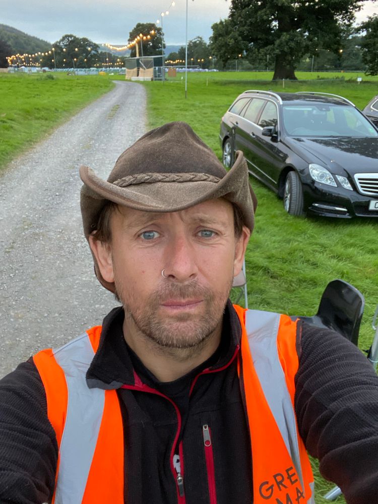 Me, stewarding at the Green Man Festival in 2021. Silly hat, tabard, slightly worried look on my face for some reason…