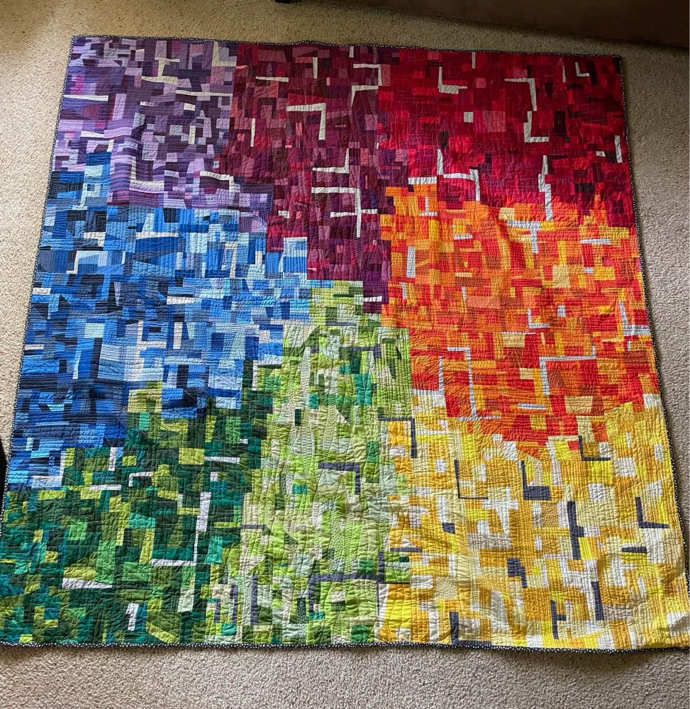 A quilt made of small squares of purple, red, orange, yellow, green, and blue.
