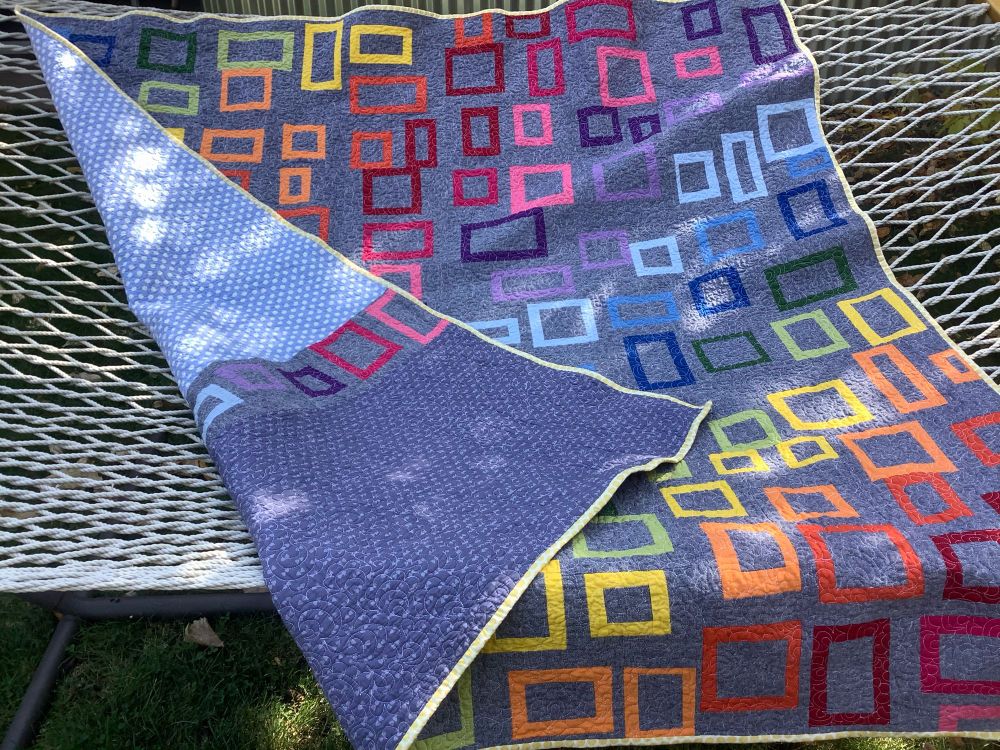 A quilt of rainbow colored boxes set in a gray background.