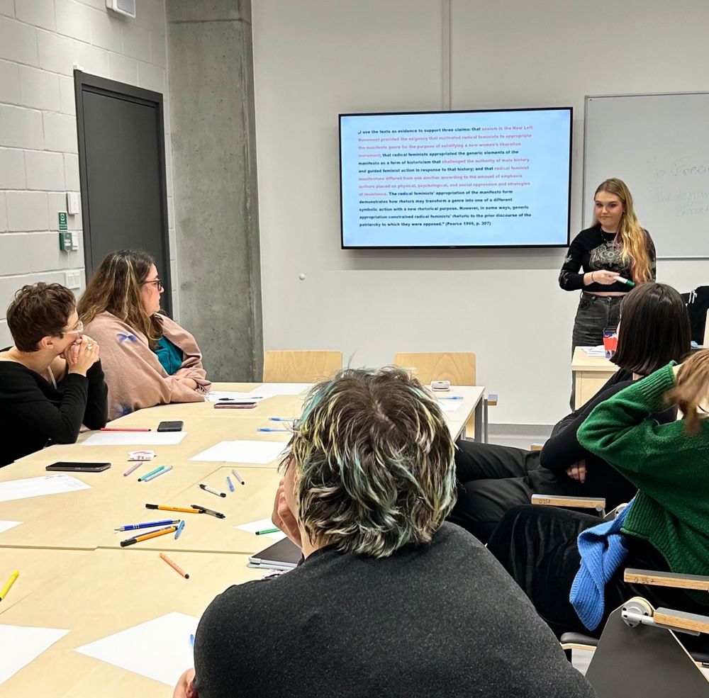 Aleksandra Julia Malinowska discussing a quote presented on the slide, there are students sitting around the workshop table.