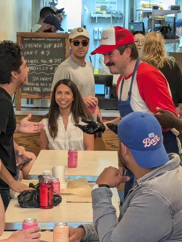 People are interacting at Salt Hank's café, with Hank himself in a red and white cap and shirt engaging with seated patrons.