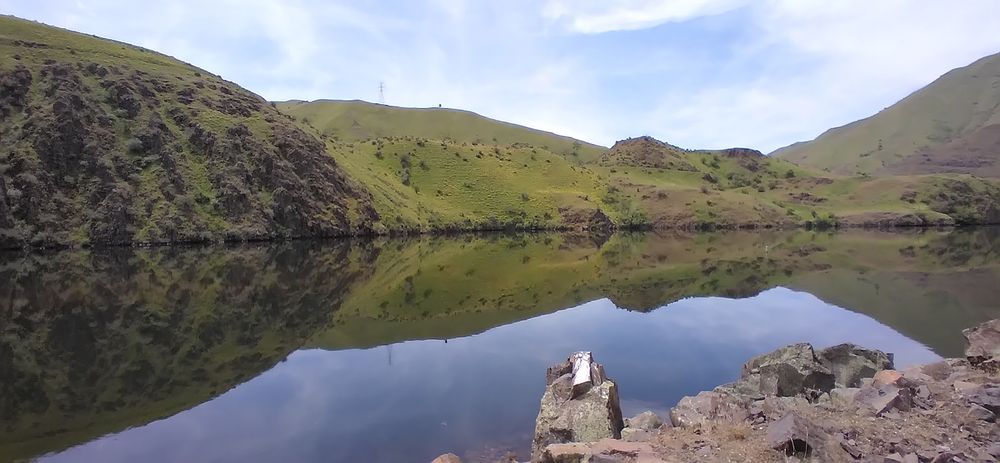 Snake River along the border of Idaho and Oregon.  The river is so still that it created an almost perfect mirror-like surface.  The low grass-covered hills are reflecting crisply on the surface of the river, creating almost an optical illusion. 