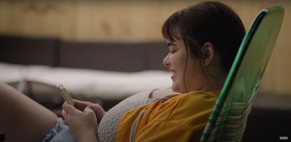 Fotograma del trailer de "Un 'like' de Bob Trevino", película producida, escrita y dirigida por Tracie Laymon en 2023, basada en sus propias experiencias
En la escena, Lily Trevino (Barbie Ferreira) sonriente viendo sus RRSS en el teléfono, tumbada en una hamaca verde con ropa veraniega
En todo el trailer no he encontrado ningún plano con Lily y Bob (John Leguizamo) juntos!