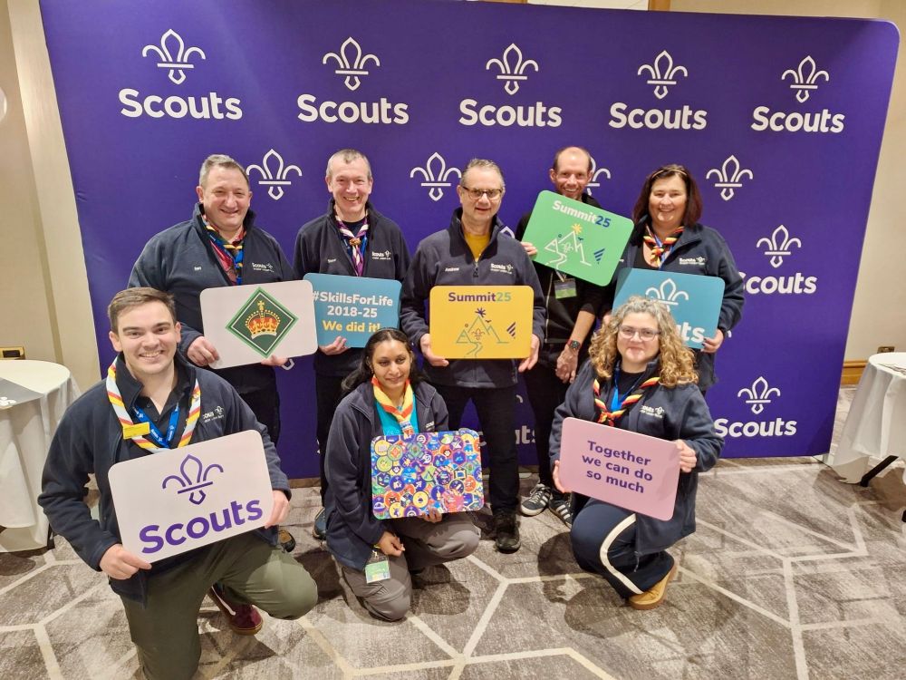 Eight people holding boards in front of a display of Scout logos