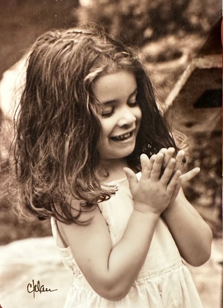 A sweet 3 year old girl of mixed race claps her hands and laughs at something.