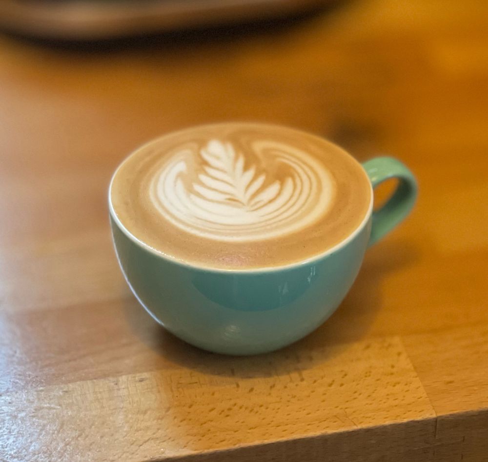 An iPhone portrait photo of my flat white from this morning. It’s a small 6oz teal mug sitting on a wooden countertop with a rosette pattern in the milk - actually quite a good pour, if I do say so myself - they’re not always this social media-worthy. 
