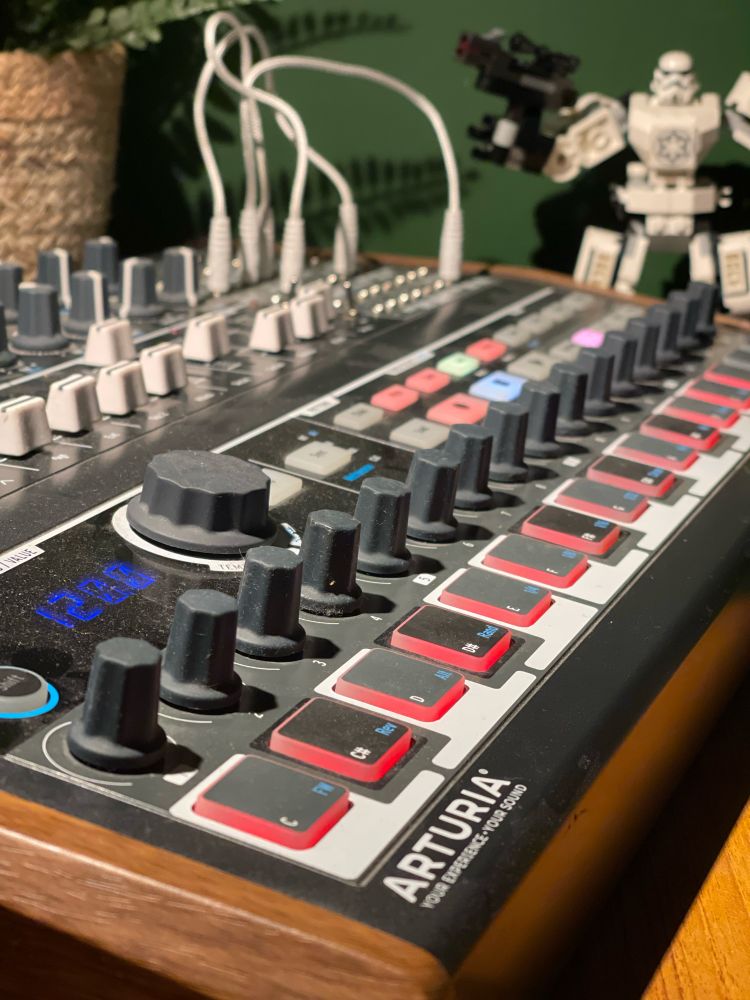 A photograph of my Arturia MiniBrute 2S synth. It’s got rows of dials and glowing buttons and a few white patch cables in the far corner. 