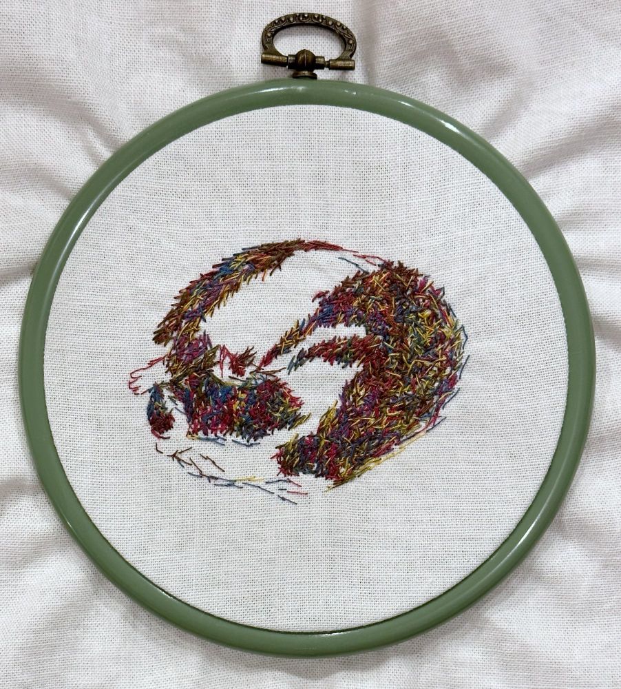 A multicolored embroidery of a cat curled up asleep. The techniques used give the piece a sketchy quality. 