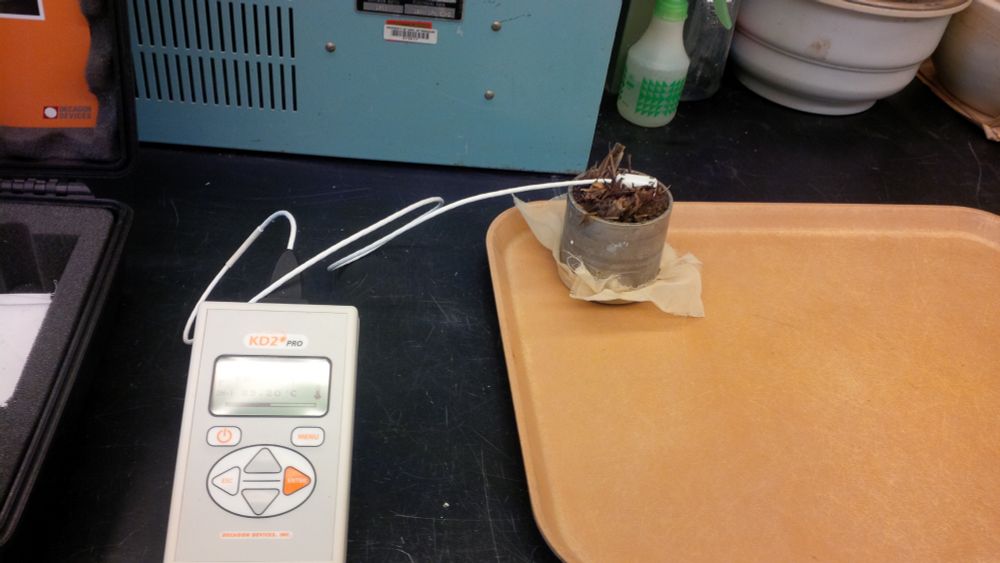 A soil sample is in a cup. A wire is inserted into the soil, attached to a KD2 Pro soil analyzer. 