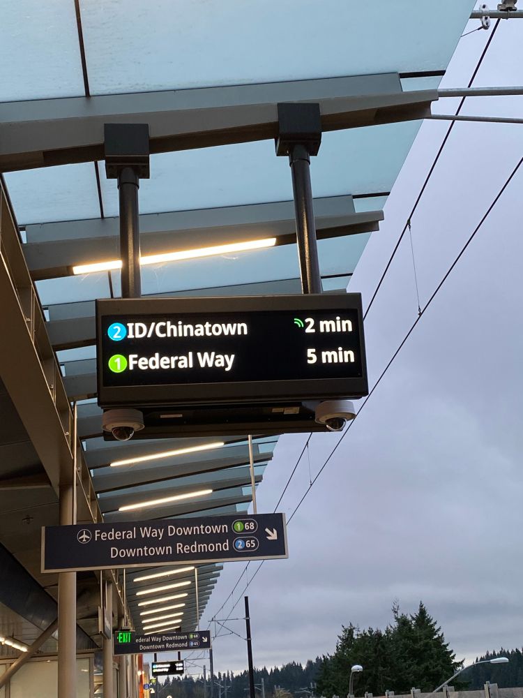 A photo of a sign at a light rail station showing arrival times for 1 Line and 2 Line trains for Sound Transit light rail. The 2 Line is a new line that will eventually connect Seattle to the Eastside.