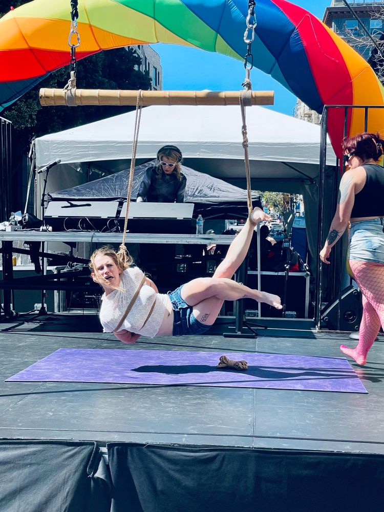 Slab_me_harder in a side suspension on stage with one ankle raised and the TK raised. 