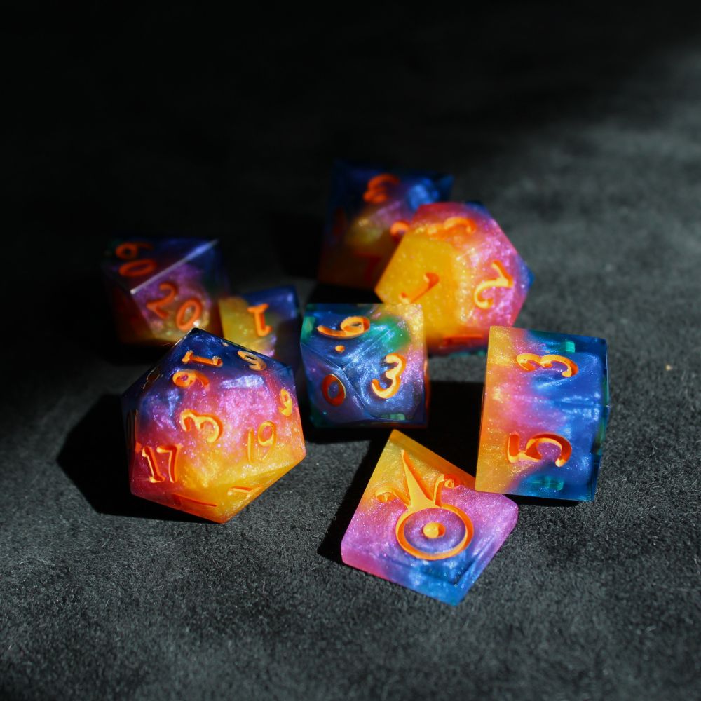 A set of dice half in shadow and half in bright sunlight. The dice fade from blue to purple to pink to yellow-orange, and have orange numbers.