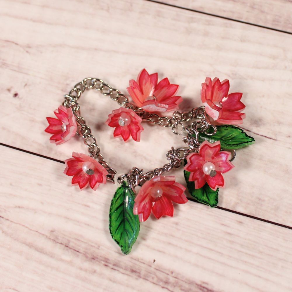 A bracelet made up of a silver chain with small pink flowers and green leaves attached to it.