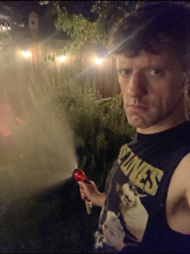Me in a black muscle t watering the rosemary and raspberries at night