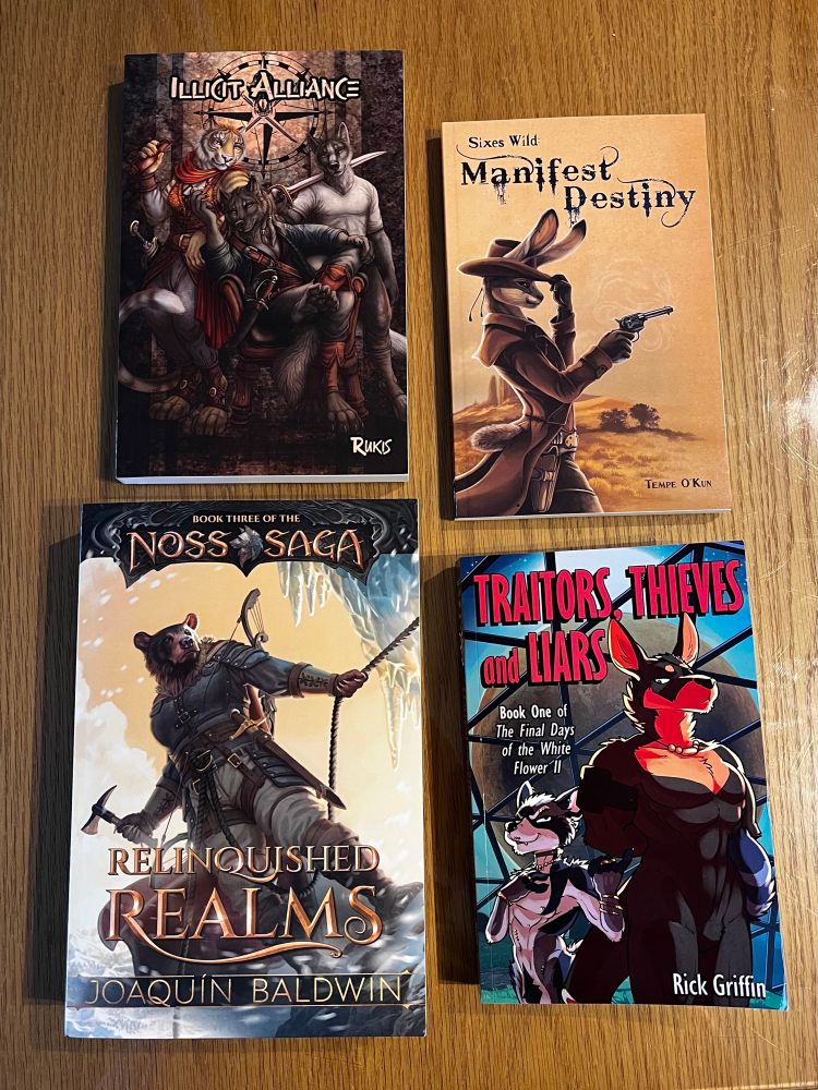 Photo of four books. “Illicit Alliance” by Rukis, “Manifest Destiny” by Tempe O’Kun, “Relinquished Realms” by Joaquin Baldwin, and “Traitors, Thieves and Liars” by Rick Griffin.