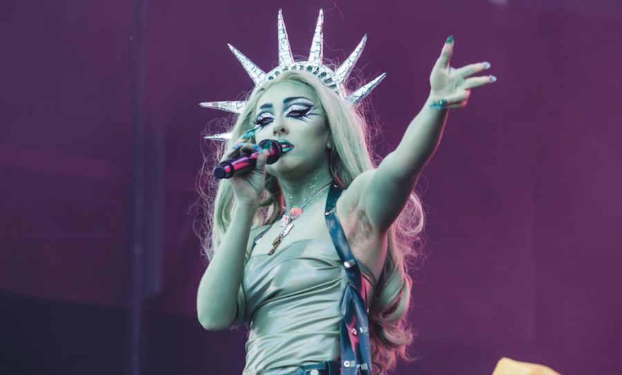 Chappell Roan performing dressed as the Statue of Liberty, with a spike crown and both a light green shirt with her skin painted match while holding the microphone to her face and her other arm extending out to the crowd