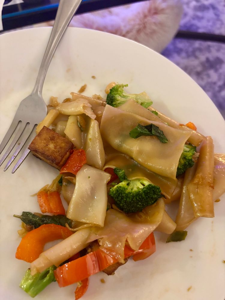 White plate with rice noodles, red bell peppers, broccoli and basil 