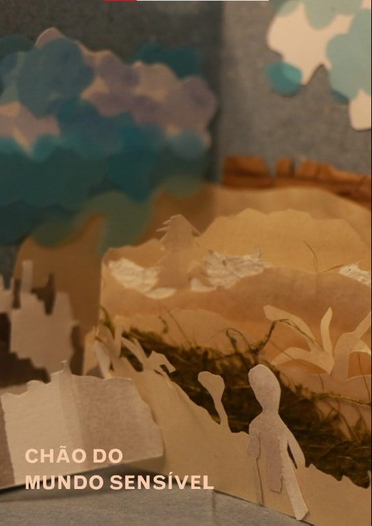 Capa de capítulo. Título "Chão do mundo sensível" sobre fotografia de parte de um livro-objeto que mostra uma paisagem com nuvens, montagens, plantas e silhuetas de pessoas, separadas em planos recortados em papéis artesanais.