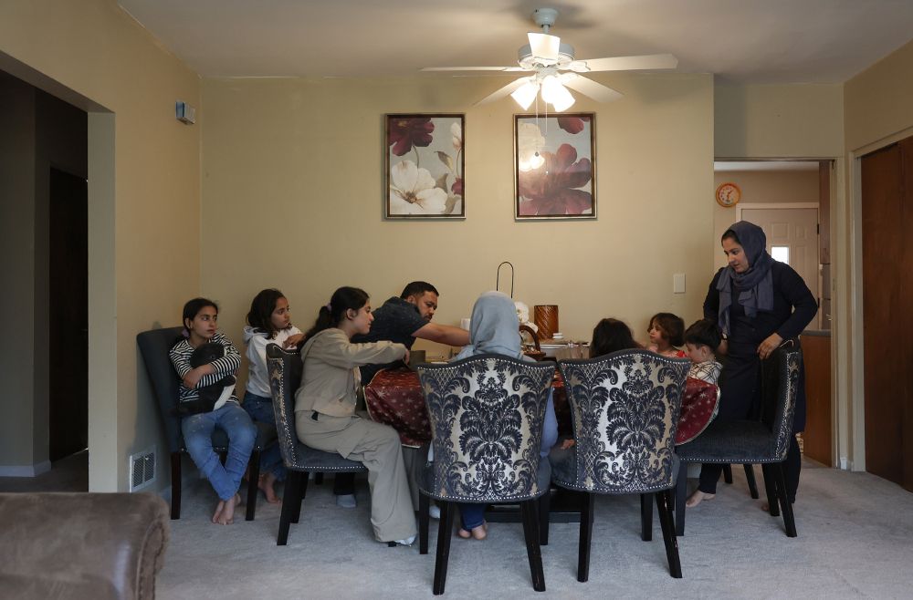 The Azizi family, including father Hamid, center left, mother Fahima, right, with their seven children, gather at the dinner table for snacks after school at their new home in the West Ridge neighborhood Friday, May 2, 2025, in Chicago. 
