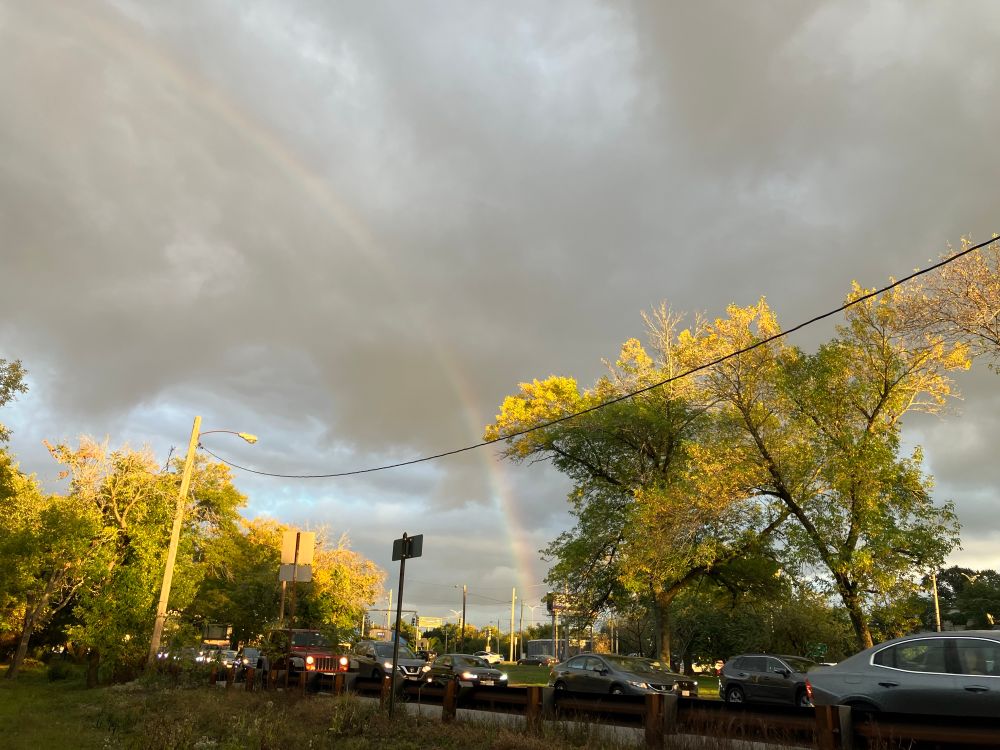 Cloudy scene with rainbow and cars in traffic. 