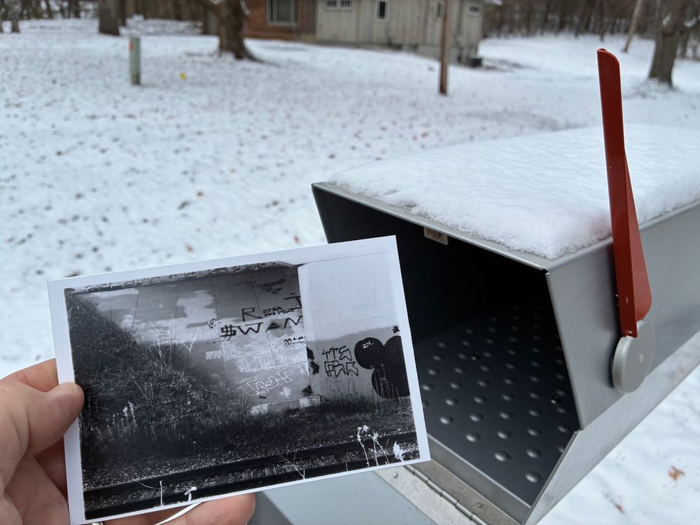 A photo of a postcard being placed into a mailbox
