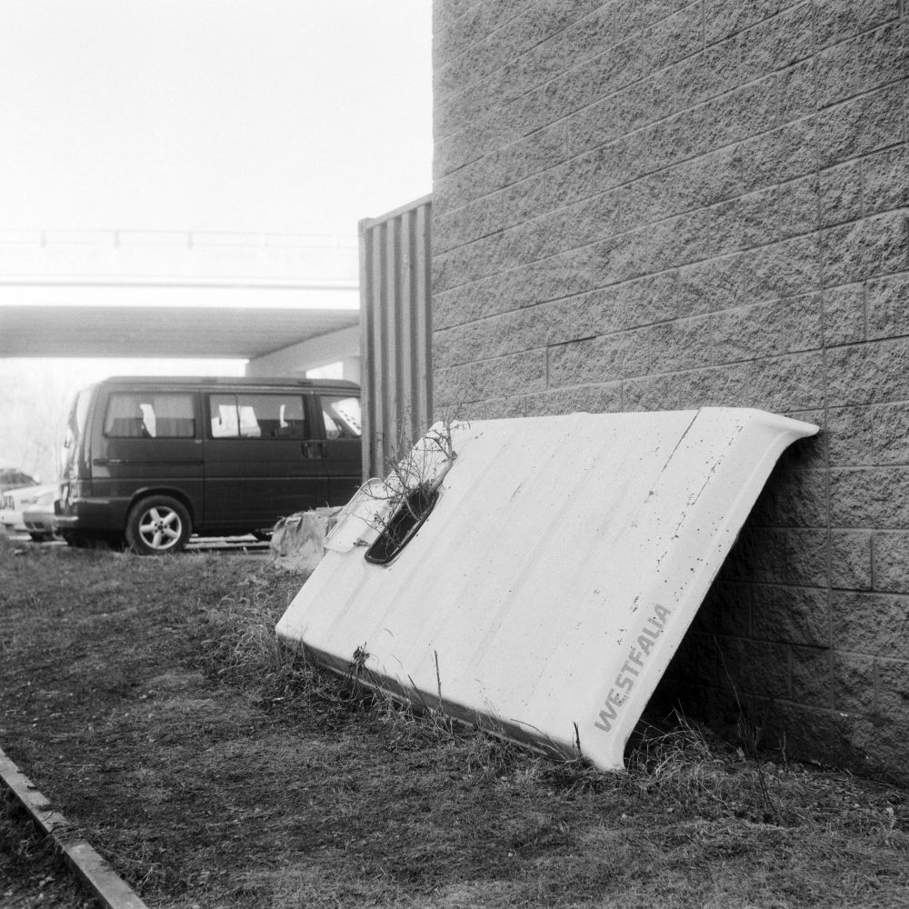 A black and white photo of the top of a Westfalia camper van leaning against the side of a building