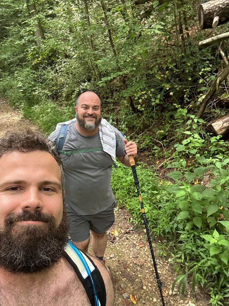 Two middle aged bearded men hiking in the woods. 