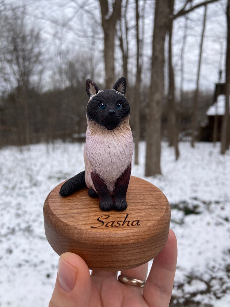 Clay sculpture of a fluffy Siamese cat on a wooden base engraved with the name 