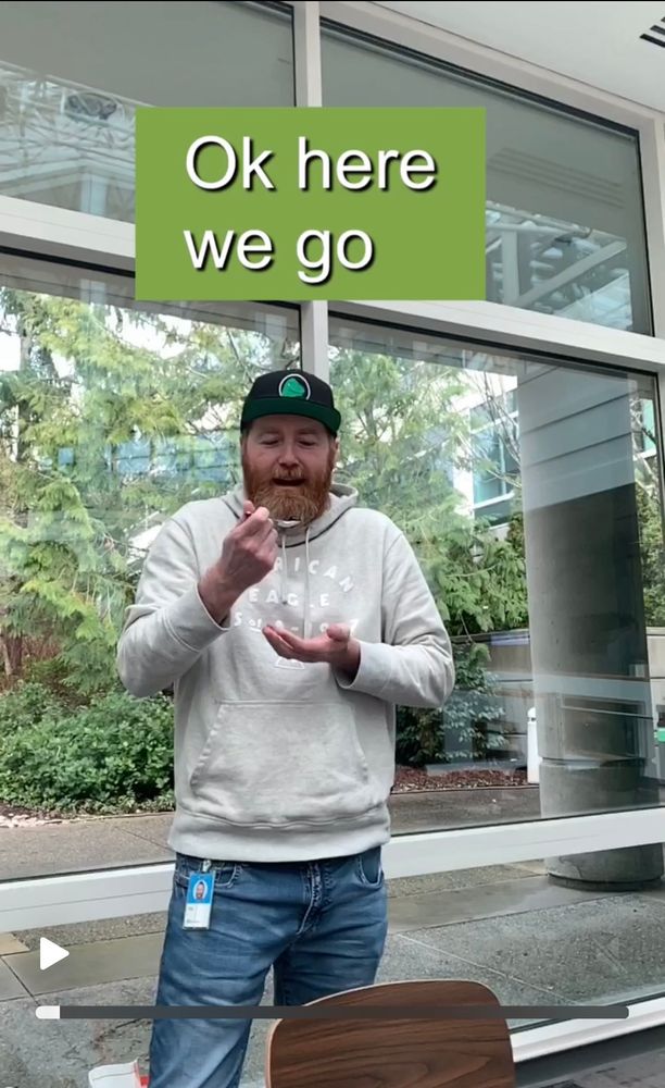 White guy standing in a cafe with a window backdrop about to eat a spoon of vegemite. Text says 