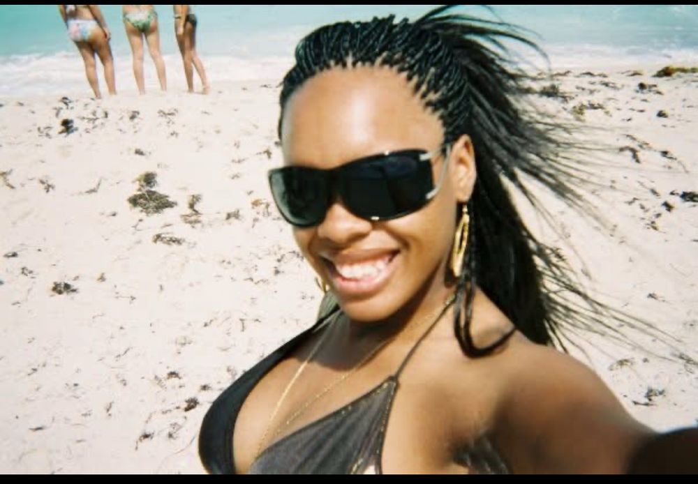 A pic of me at 21 on the beach in Miami with oversized sunglasses, micro braids, and a metallic bikini top