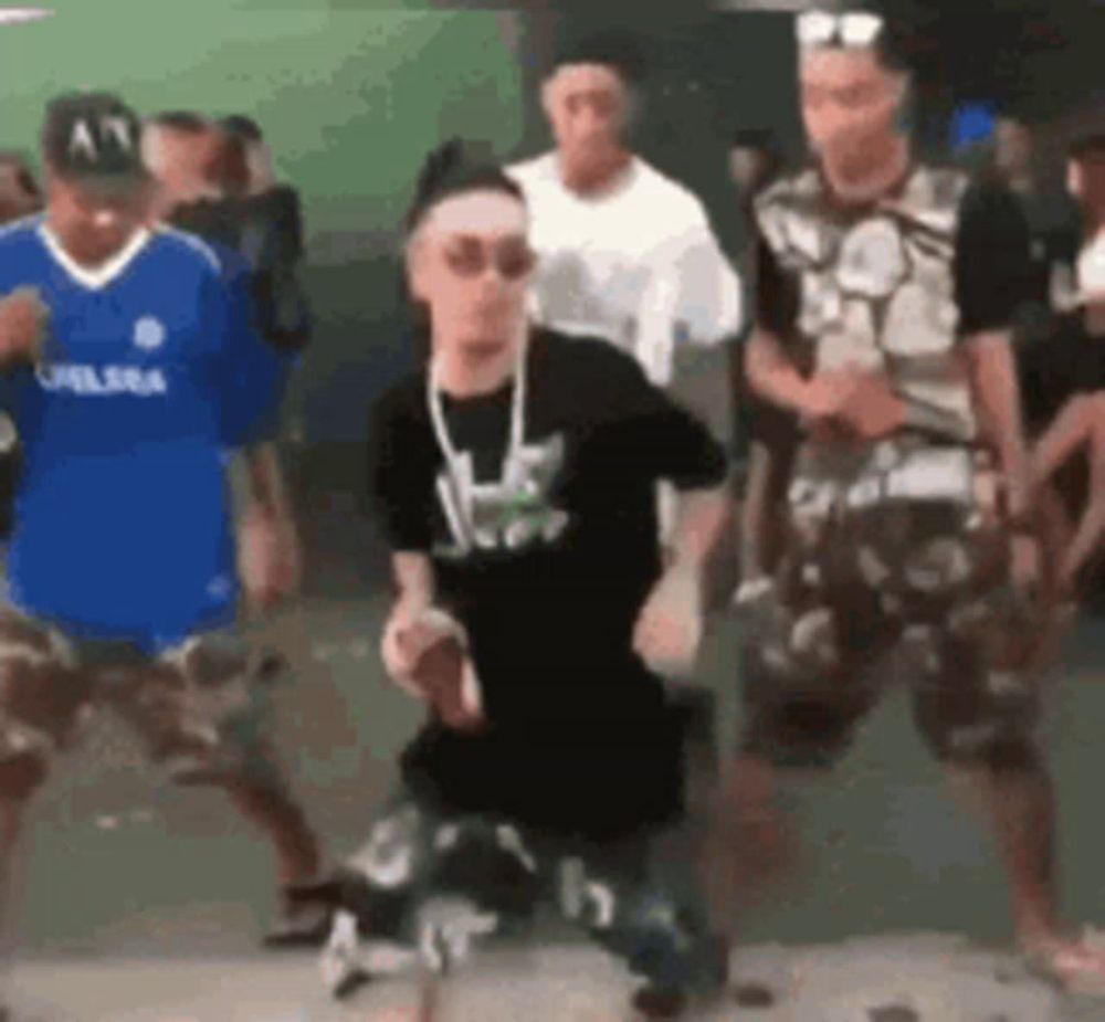 a group of men are dancing in front of a crowd . one of the men is wearing a blue chelsea jersey .