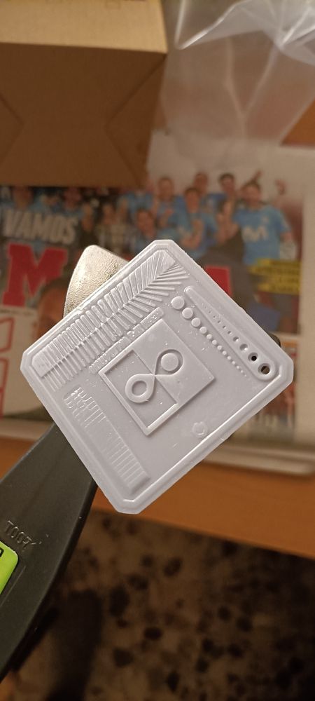 Forma gris cuadrada con multitud de rayas, puntos, agujeros y dibujos de color gris sostenido en una espátula negra 