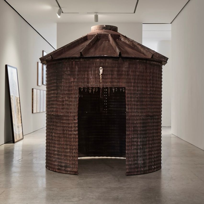 gallery photo of a round, artist-distressed farm bin with a doorway cut out, altogether made of rusty corrugated steel. It’s about 12’ tall with an 8’ diameter.